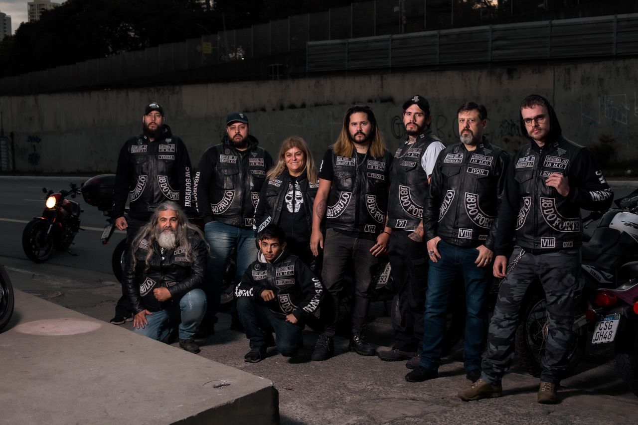 A diverse group of bikers in leather gear posing near their motorcycles on an urban street.